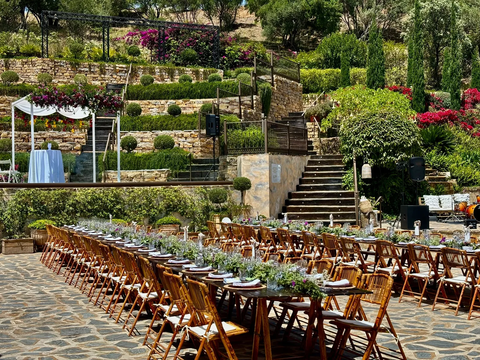 Finca con jardines escalonados y buganvillas — montaje de mesas largas junto al altar bajo arco blanco.