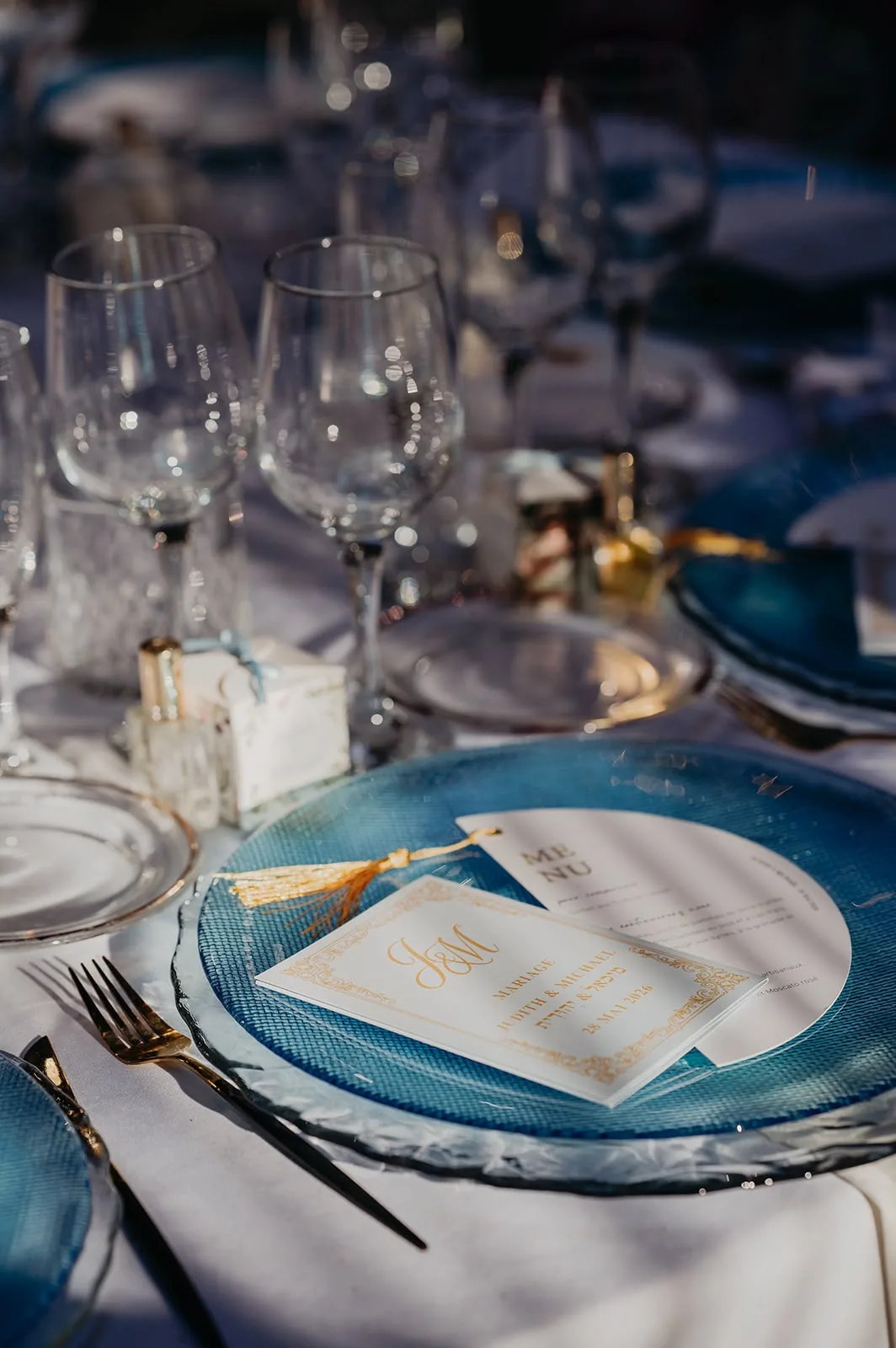 Detalle de mesa con bajoplato azul, copas de cristal y menú personalizado en boda kosher