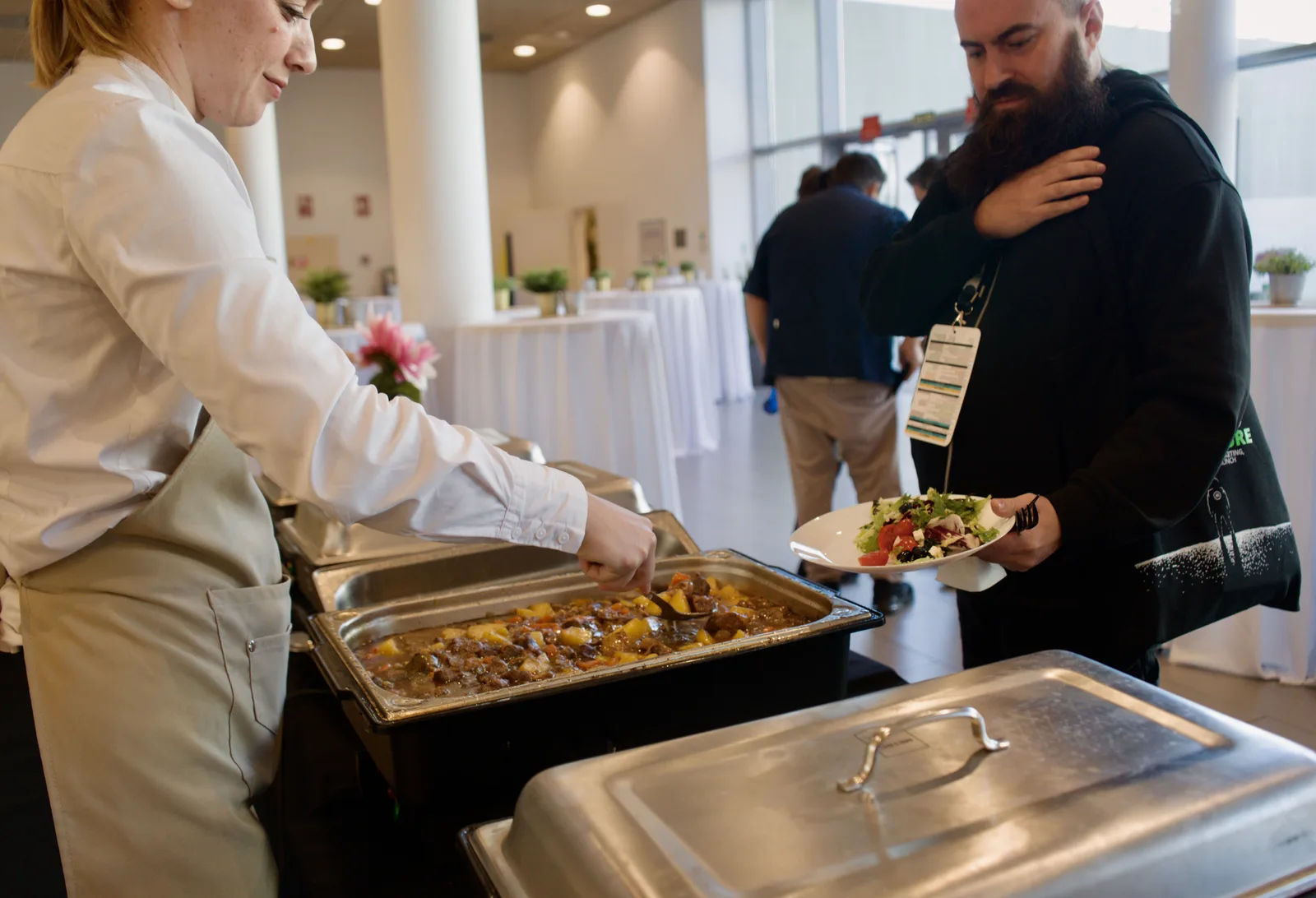 Servidora SmartCatering sirviendo plato en buffet de congreso con sala llena de asistentes
