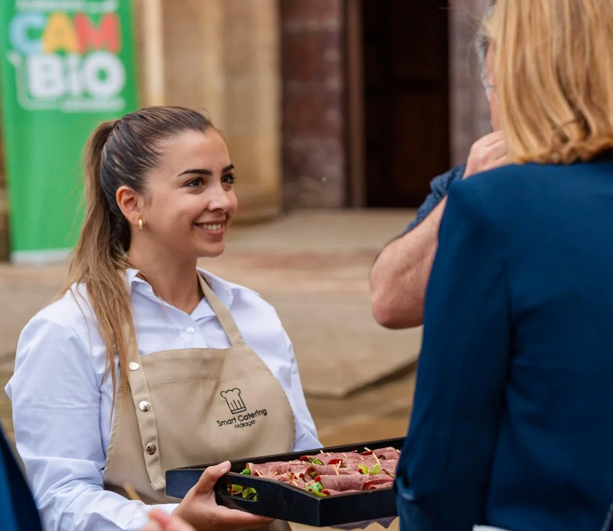 Camarera de SmartCatering sirviendo bandeja de canapés en el patio de un evento