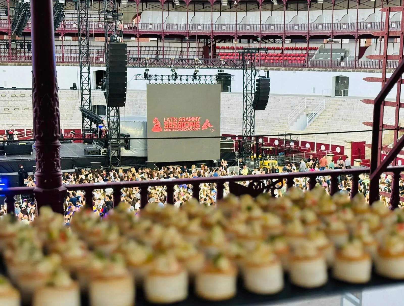 Bandeja de canapés en primer plano con el escenario de Latin Grammy Sessions en la plaza de toros al fondo