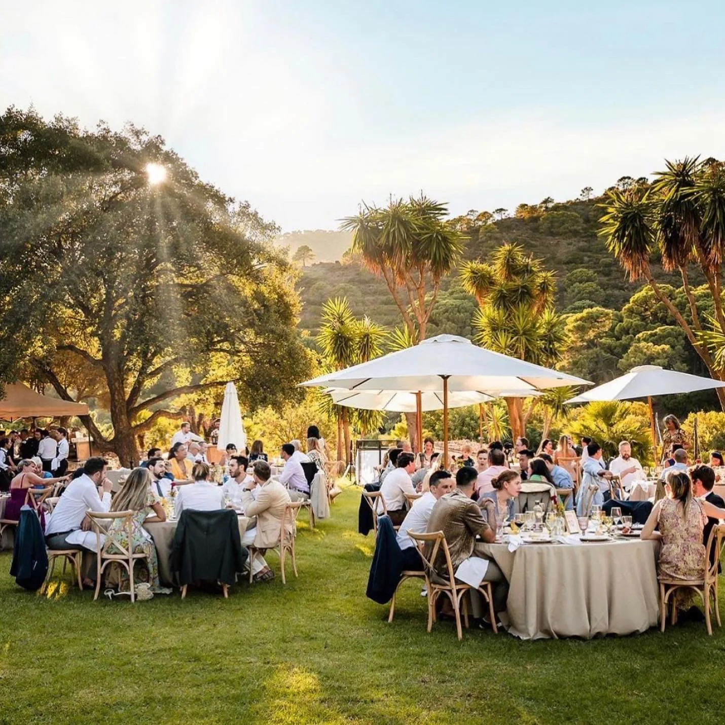 Golden-hour outdoor wedding dinner on the Costa del Sol, round tables with beige linens and cross-back chairs under white parasols