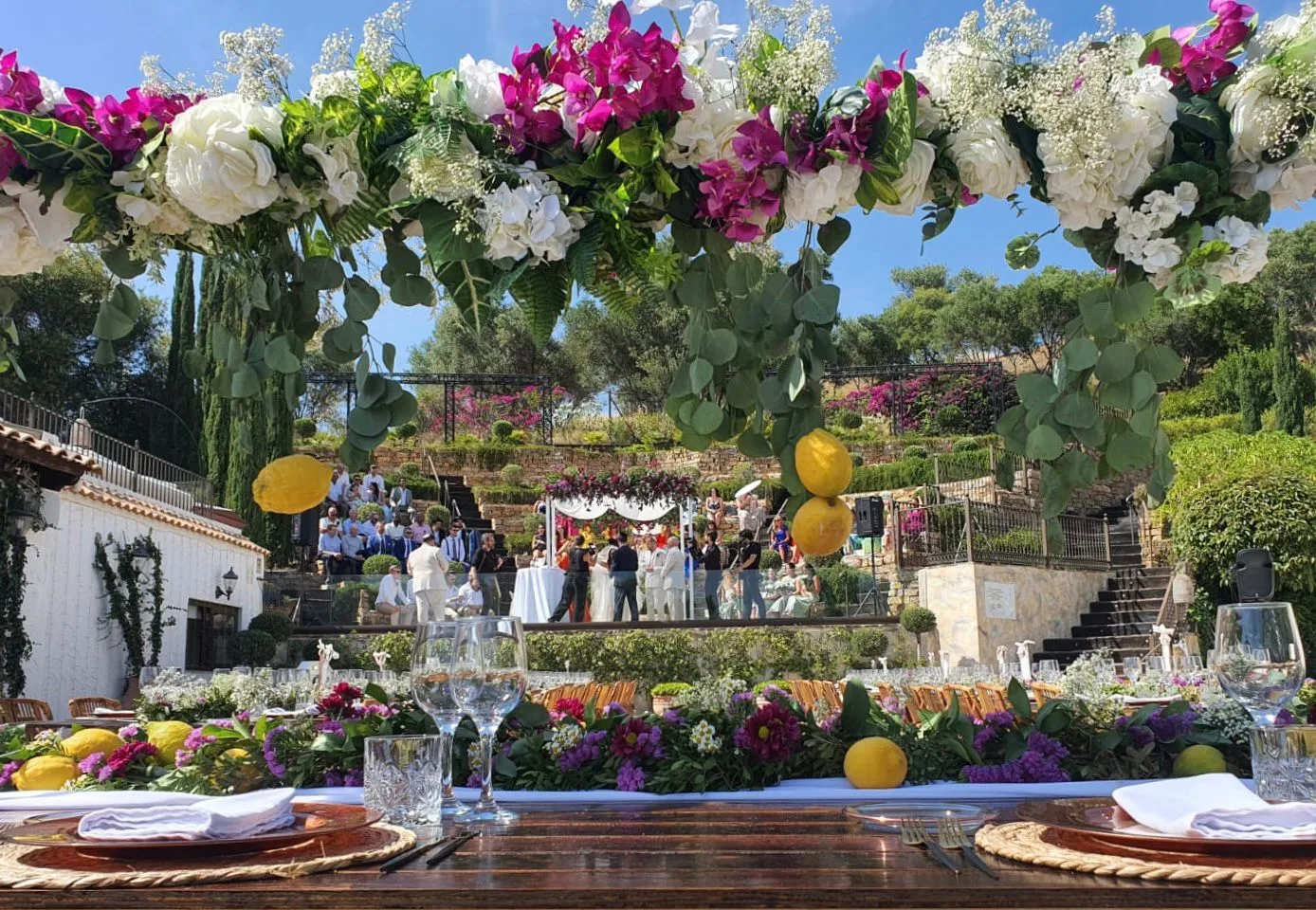 Bougainvillea and rose floral arch framing a long imperial banquet table with rattan chairs at an Andalusian finca