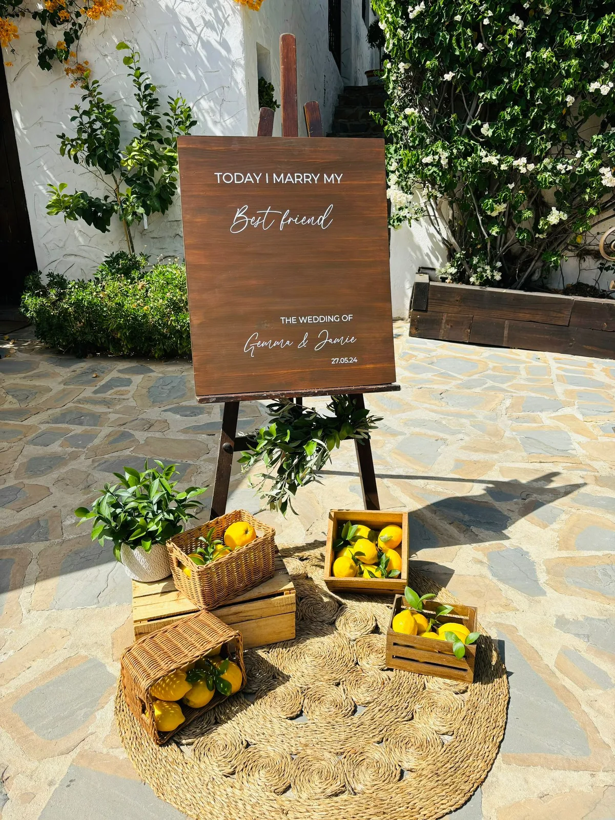 Rustic wooden easel with a handwritten destination wedding welcome sign and lemon-basket decorations at an outdoor Costa del Sol finca