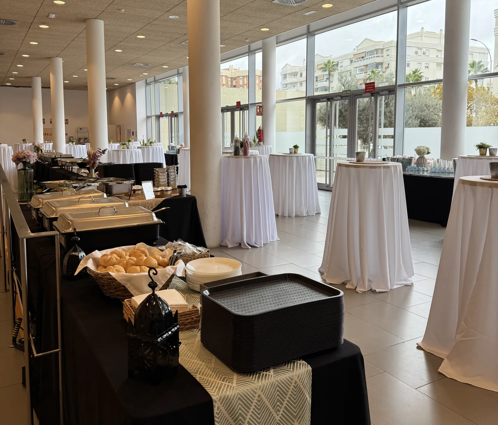 Montaje completo de buffet en sala de congresos: chafing dishes y mesas altas con mantel blanco