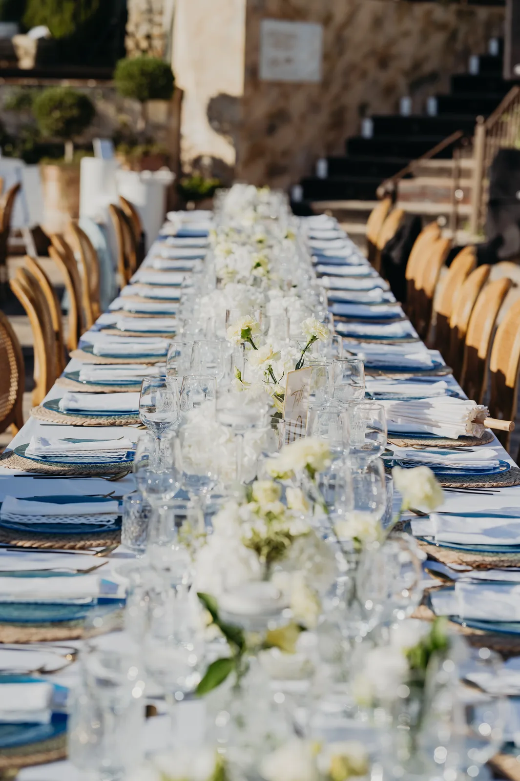Imperial banquet table with blue glass charger plates, continuous white floral runner and stone staircase, kosher wedding in Málaga